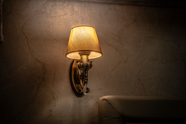 A brass wall sconce glowing against a dark plaster wall. Photo by Александр on Pexels