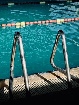 Close-up of swimming pool ladder with calm blue water, offering a serene summer atmosphere.