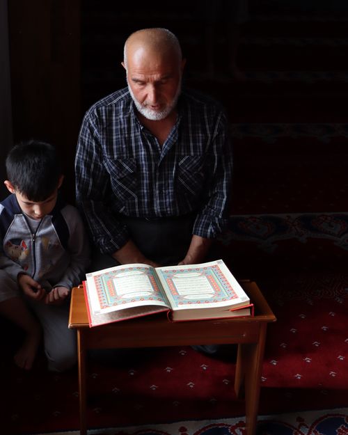 Free A father and son engaged in prayer with the Quran inside a mosque in Konya, Türkiye. Stock Photo