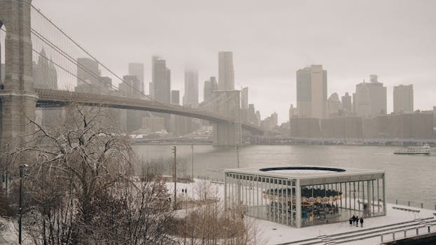 Winter view of Brooklyn Bridge and Manhattan skyline with snow-covered Jane's Carousel.
