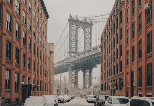 A classic view of the Manhattan Bridge framed by red brick buildings during a snowy winter day in New York City.