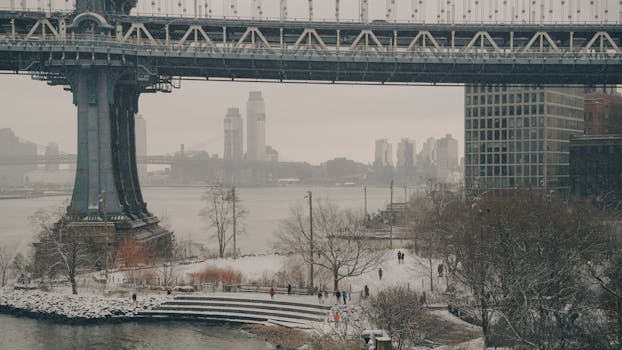 A serene winter scene of the Manhattan Bridge with snow-covered ground in New York City.