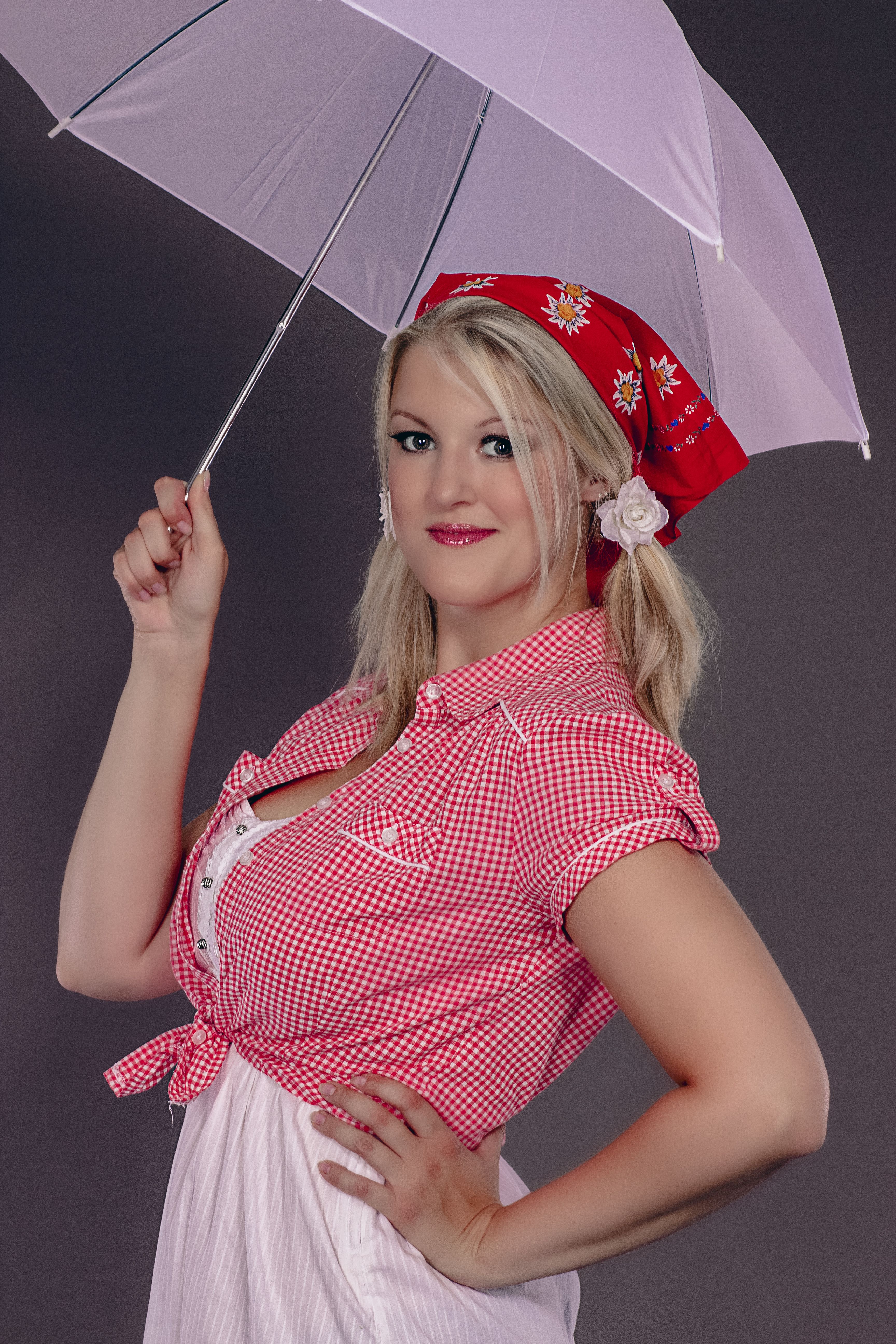 Smiling woman in vintage attire holding an umbrella against a gray backdrop.