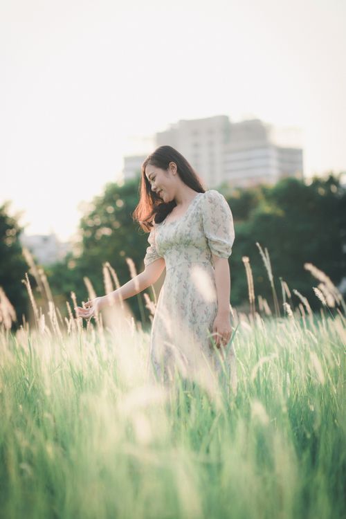 Free A woman in a floral dress enjoys a sunny day in a green field near a cityscape. Stock Photo
