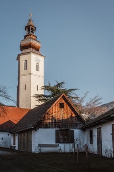 A scenic view of a rustic church tower in an Austrian village, surrounded by serene countryside.