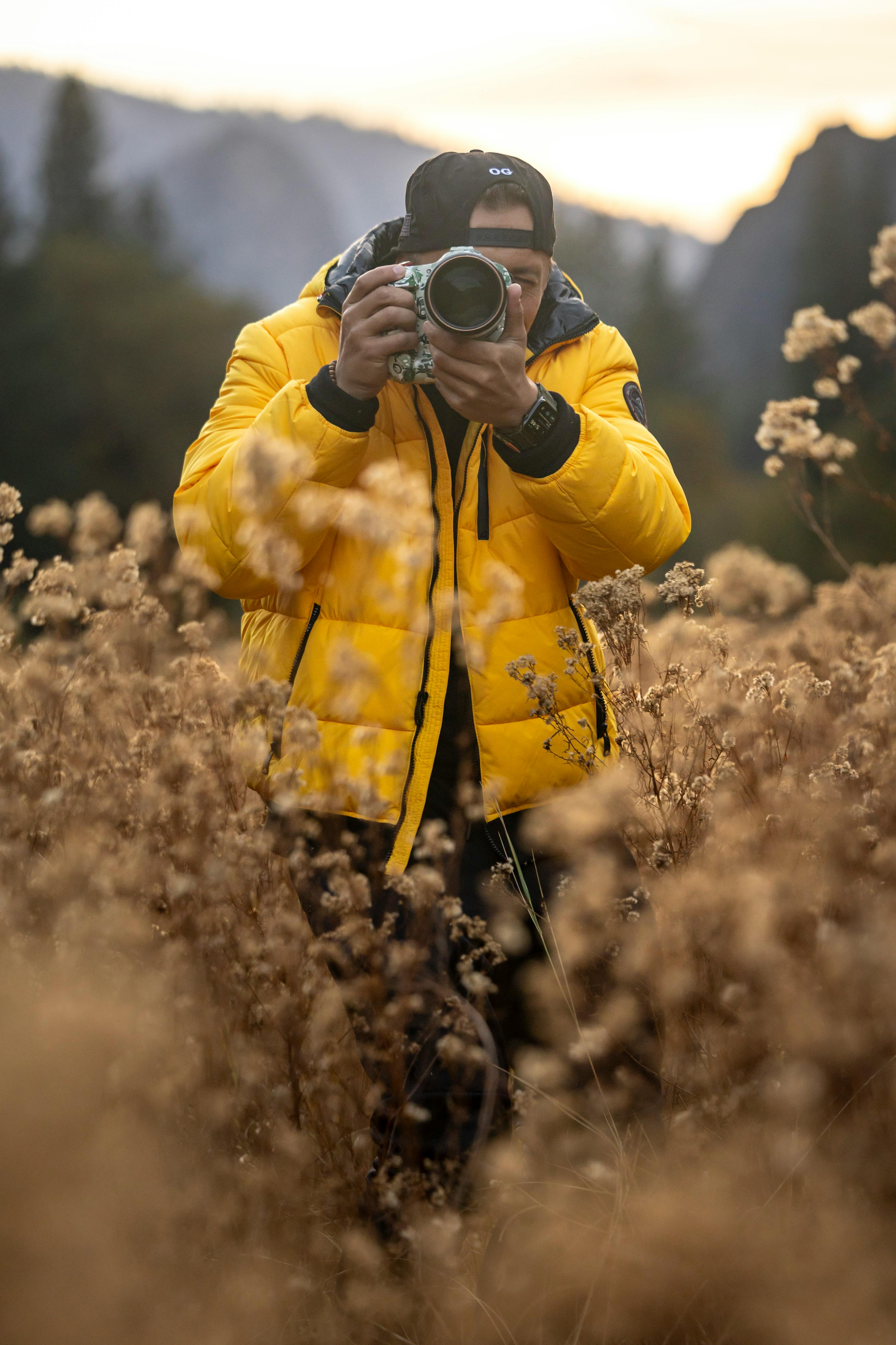 A photographer in a yellow jacket takes photos in a scenic autumn field.