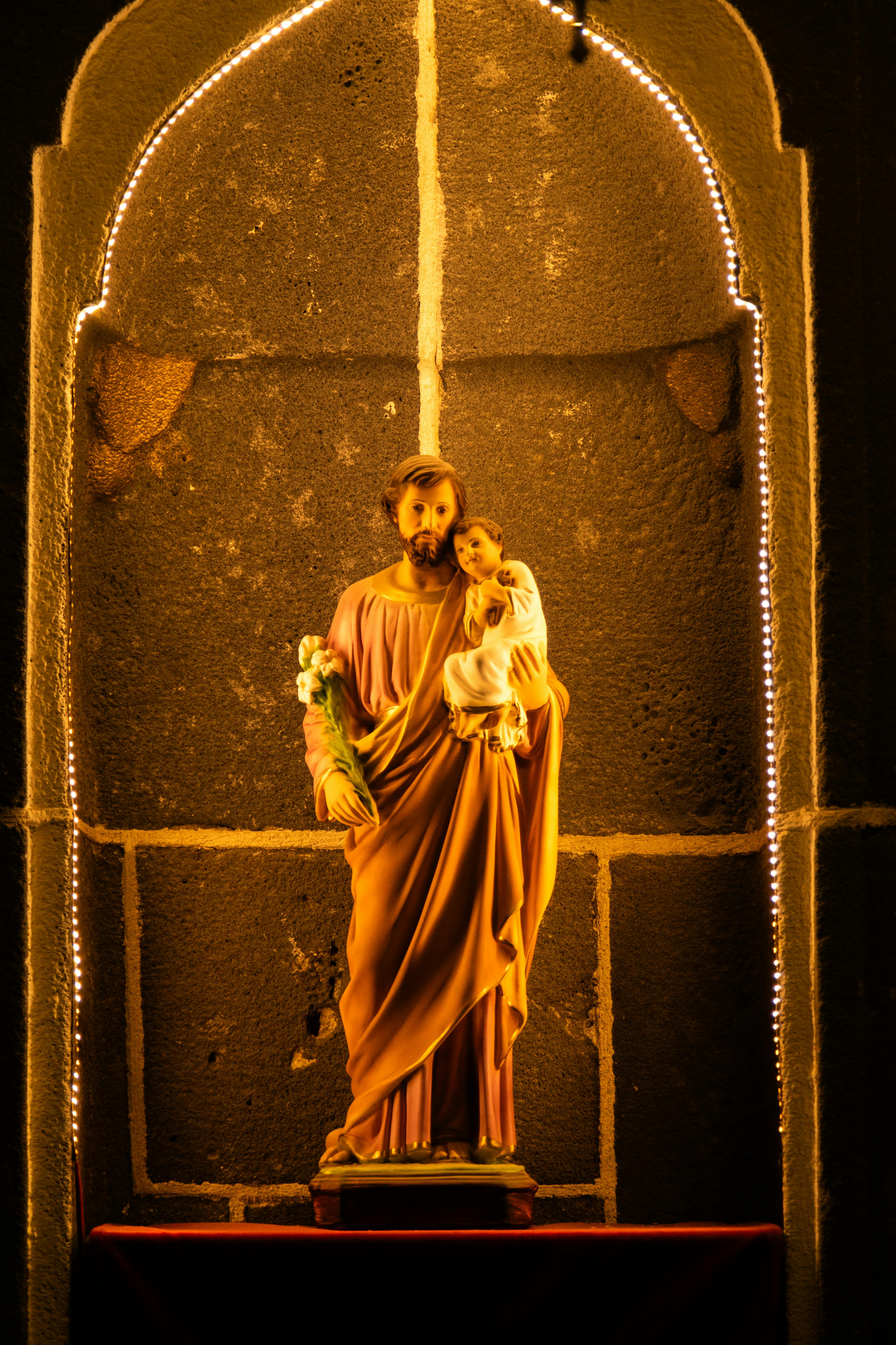 A beautifully lit religious statue in an arched niche with soft lighting, evoking a serene mood.