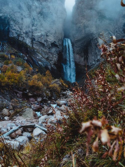 Free A dramatic waterfall cascades in a misty canyon surrounded by autumn foliage. Stock Photo
