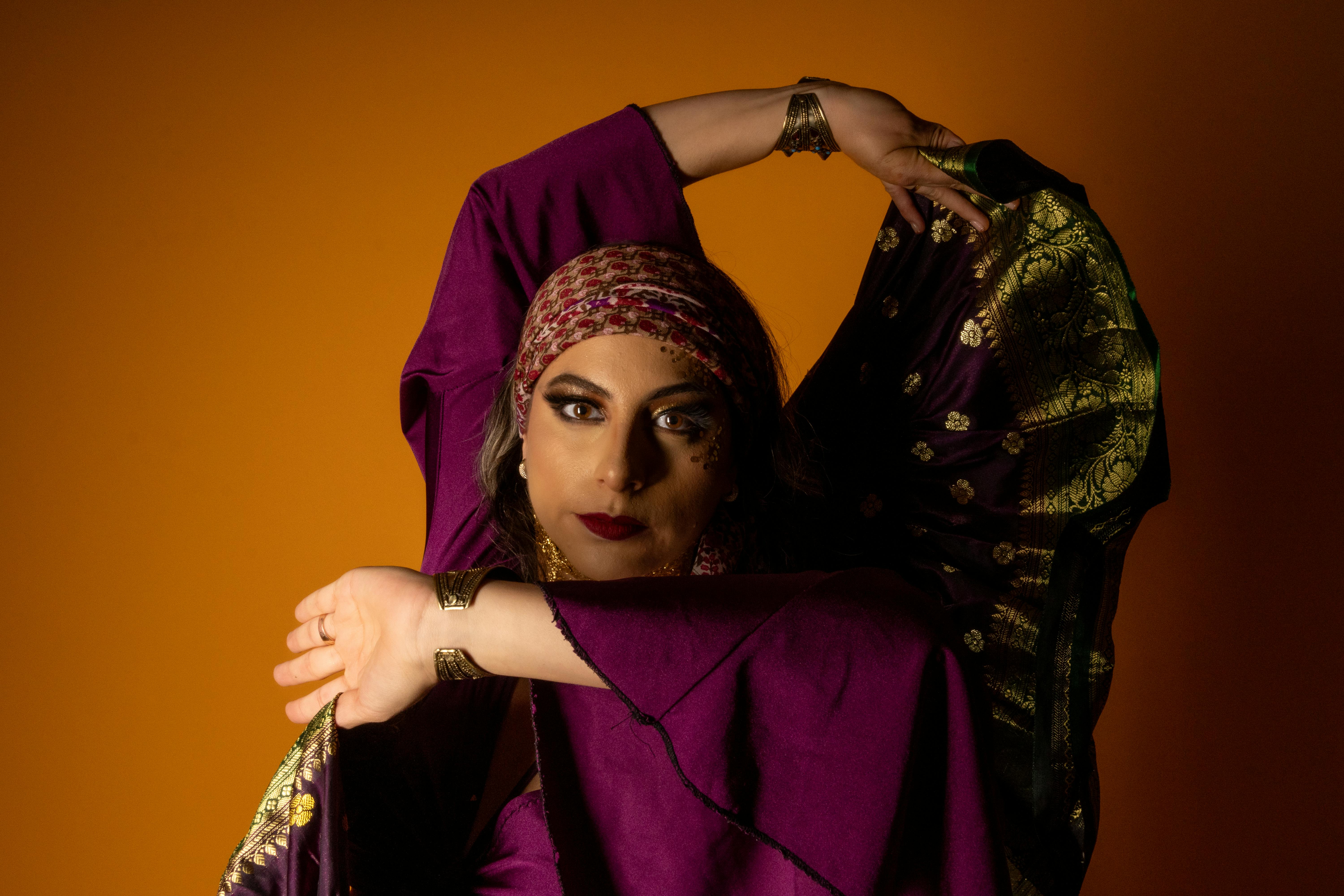 A vibrant portrait of a gypsy dancer in traditional attire striking an expressive pose against an orange background.