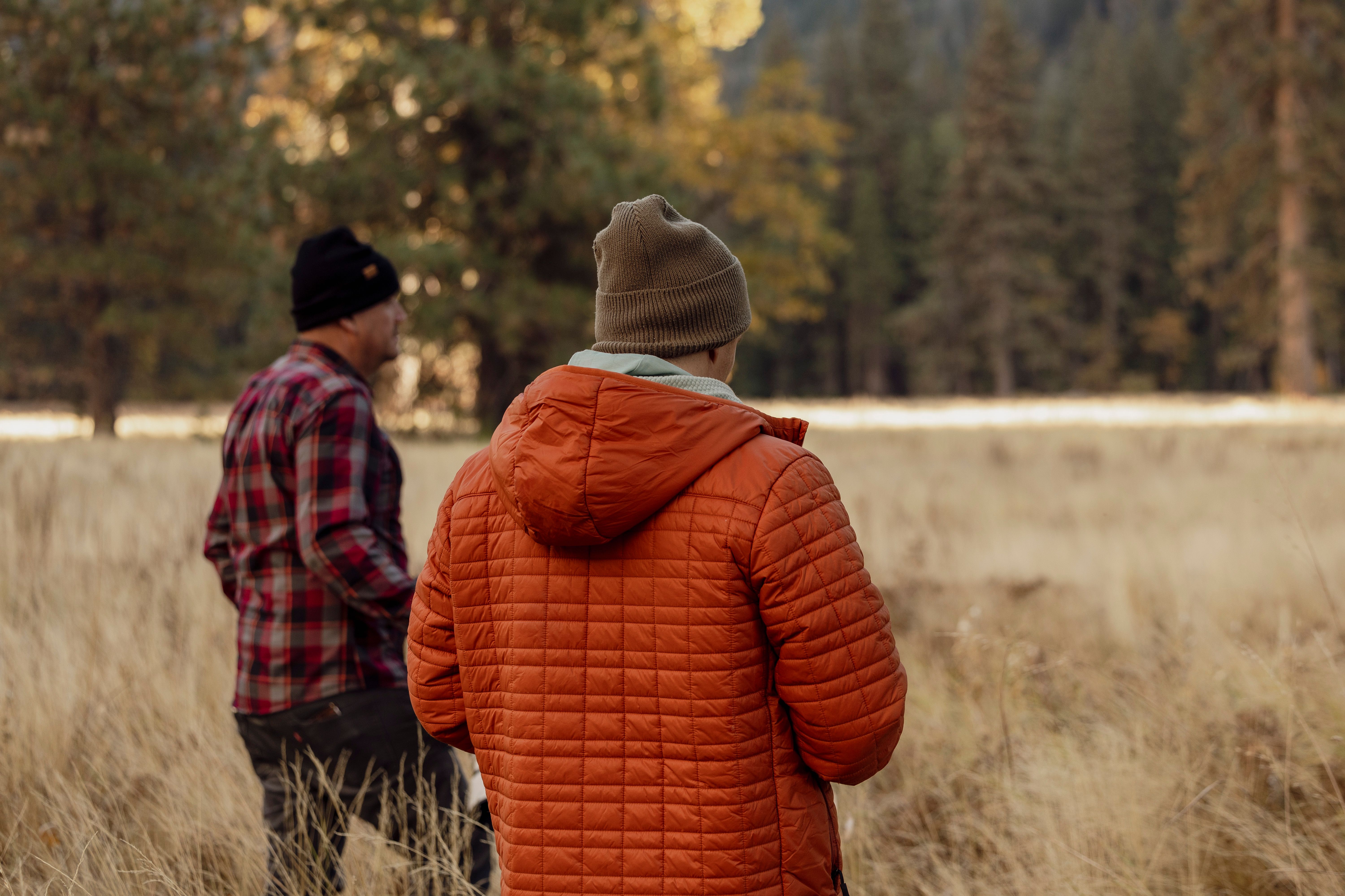 Two spectators in an insulated jacket and flannel walking a golden autumn field on a cold morning