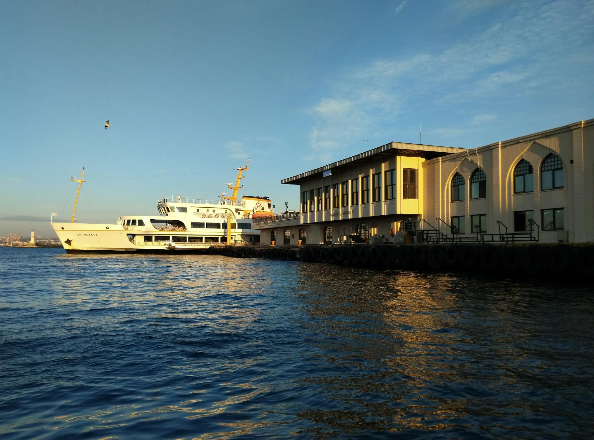 A ferry docked at a waterfront terminal at sunset, with golden reflections on the water.