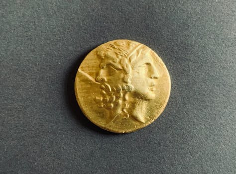 Close-up of an ancient golden coin with two faces on a dark background.
