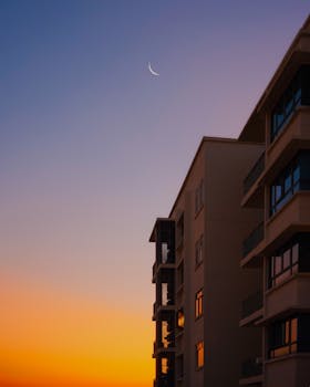 Modern building in Kuala Lumpur during sunrise with crescent moon visible in the sky.
