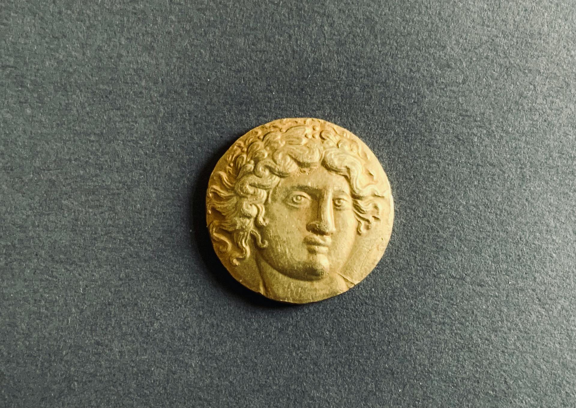 Close-up of an ancient Greek coin featuring a deity or mythological figure portrait on a dark background.