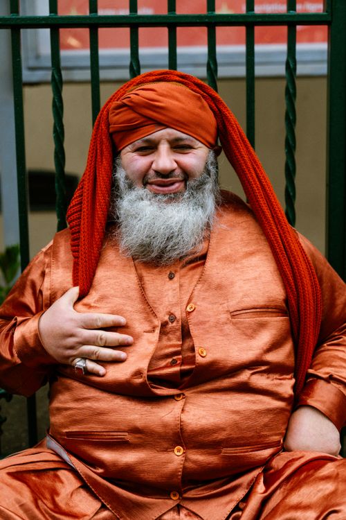 Free Cultural portrait of a smiling man wearing orange traditional attire and turban seated outdoors. Stock Photo