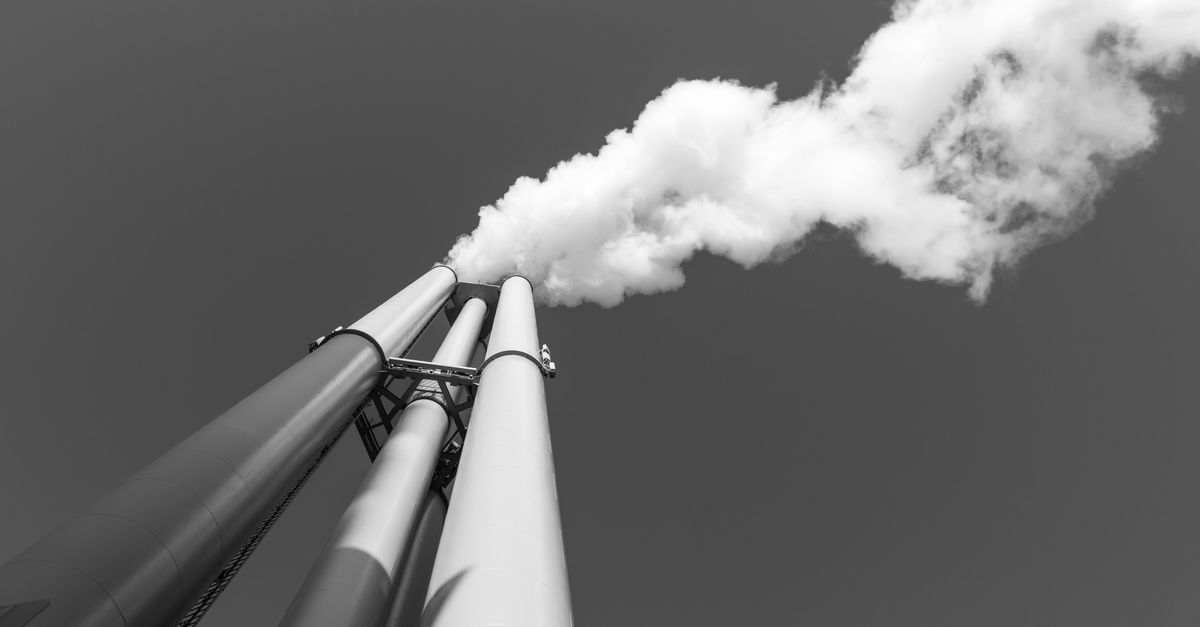 Black and white image of a smokestack with smoke against a clear sky in Hamburg.