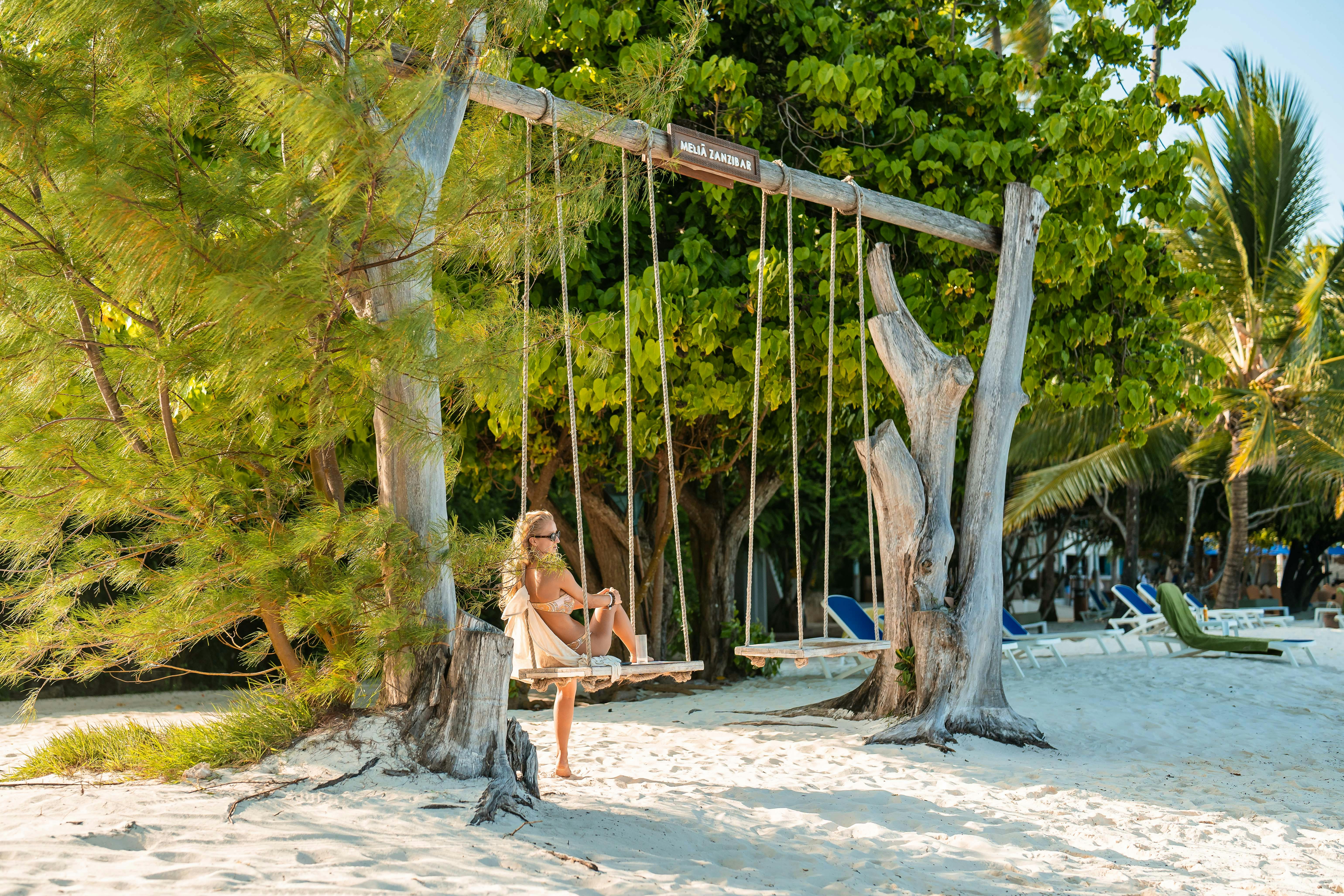 Woman enjoying a sunny day on a beach swing beneath palm trees in Zanzibar.