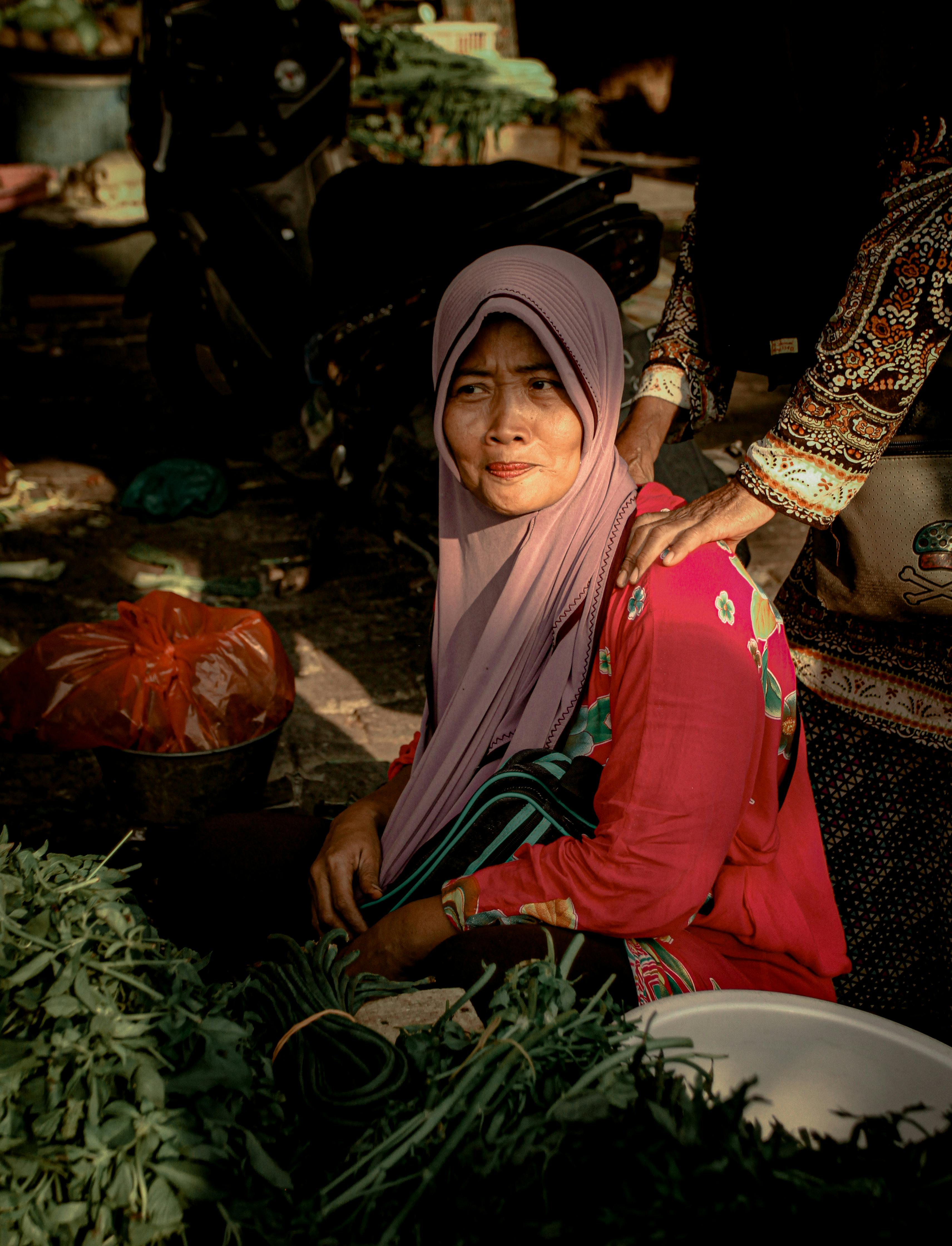 woman wearing pink hijab in the market place selling vegetables getting a shoulder massage