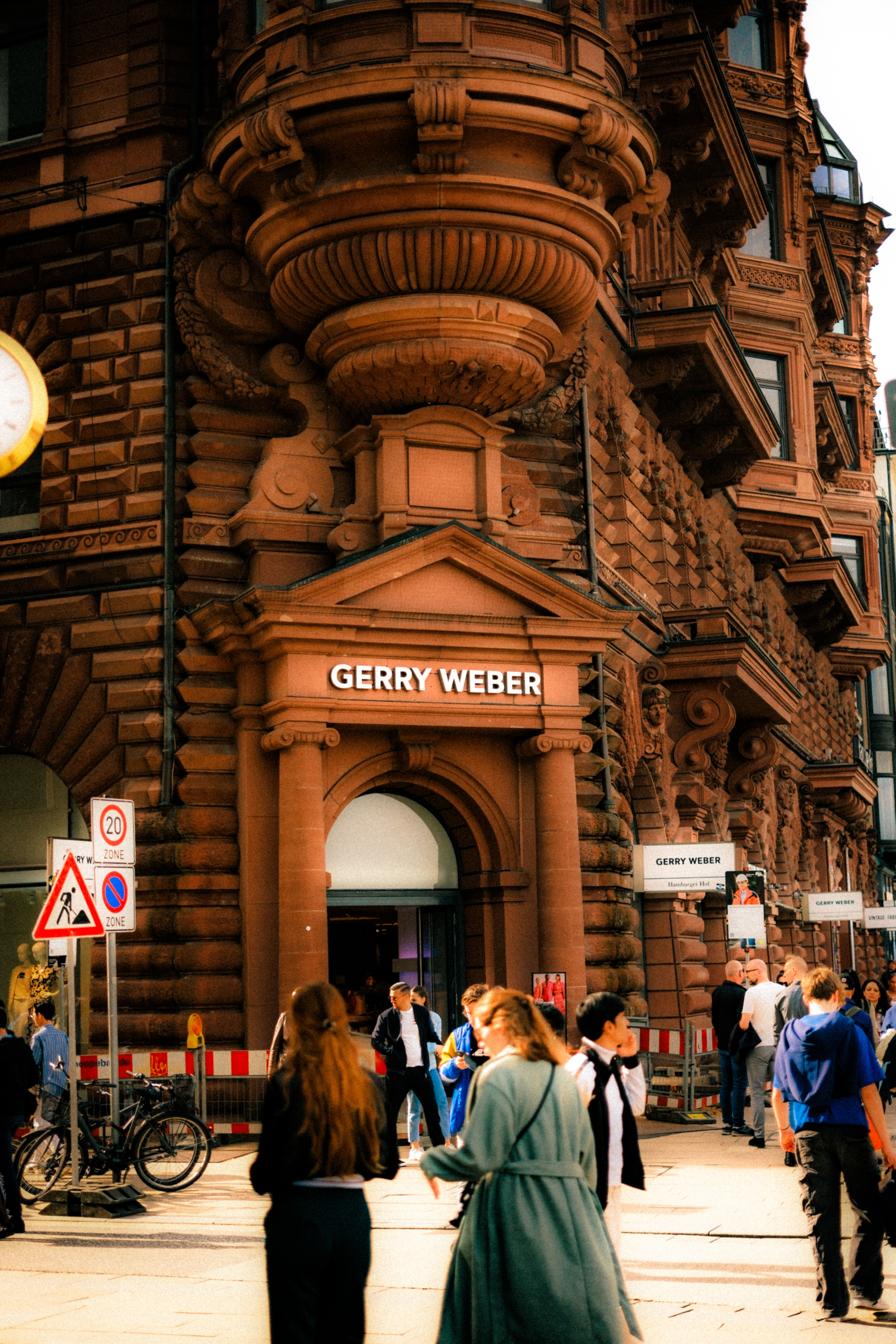 People walking near historic architecture and Gerry Weber store.
