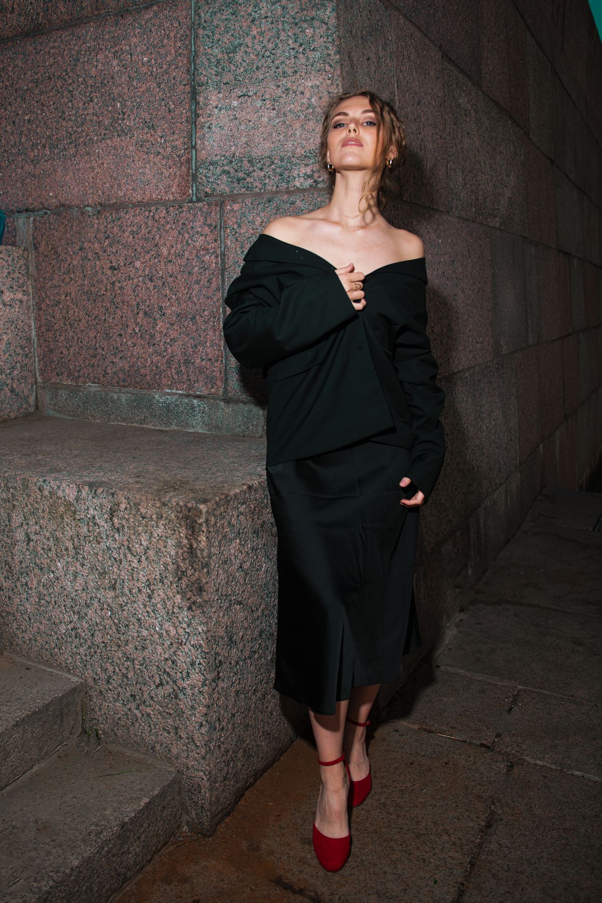 An elegant woman in an evening dress by a stone wall — the statement off-shoulder