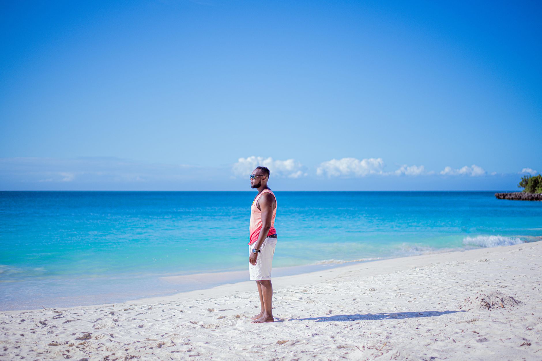A man stands on a serene sandy beach in Tanzania, gazing at the clear blue ocean.