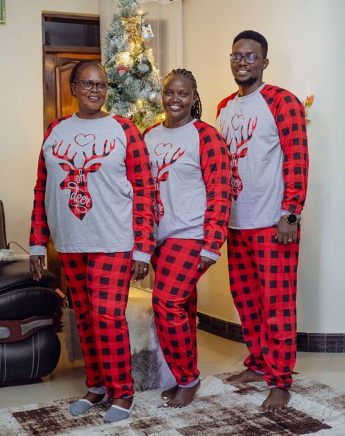 Free Family wearing matching Christmas pajamas by a decorated tree indoors. Stock Photo