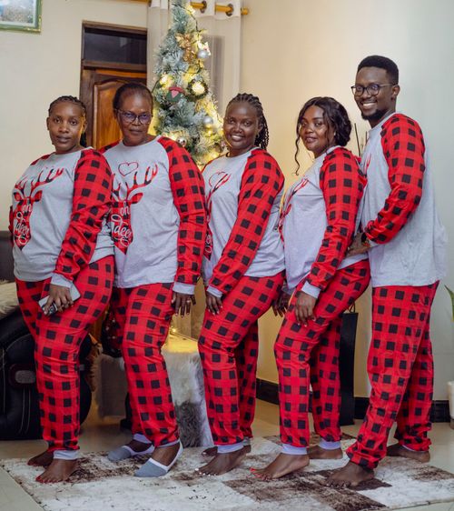 Free A joyful family poses indoors in matching Christmas pajamas by a decorated tree. Stock Photo