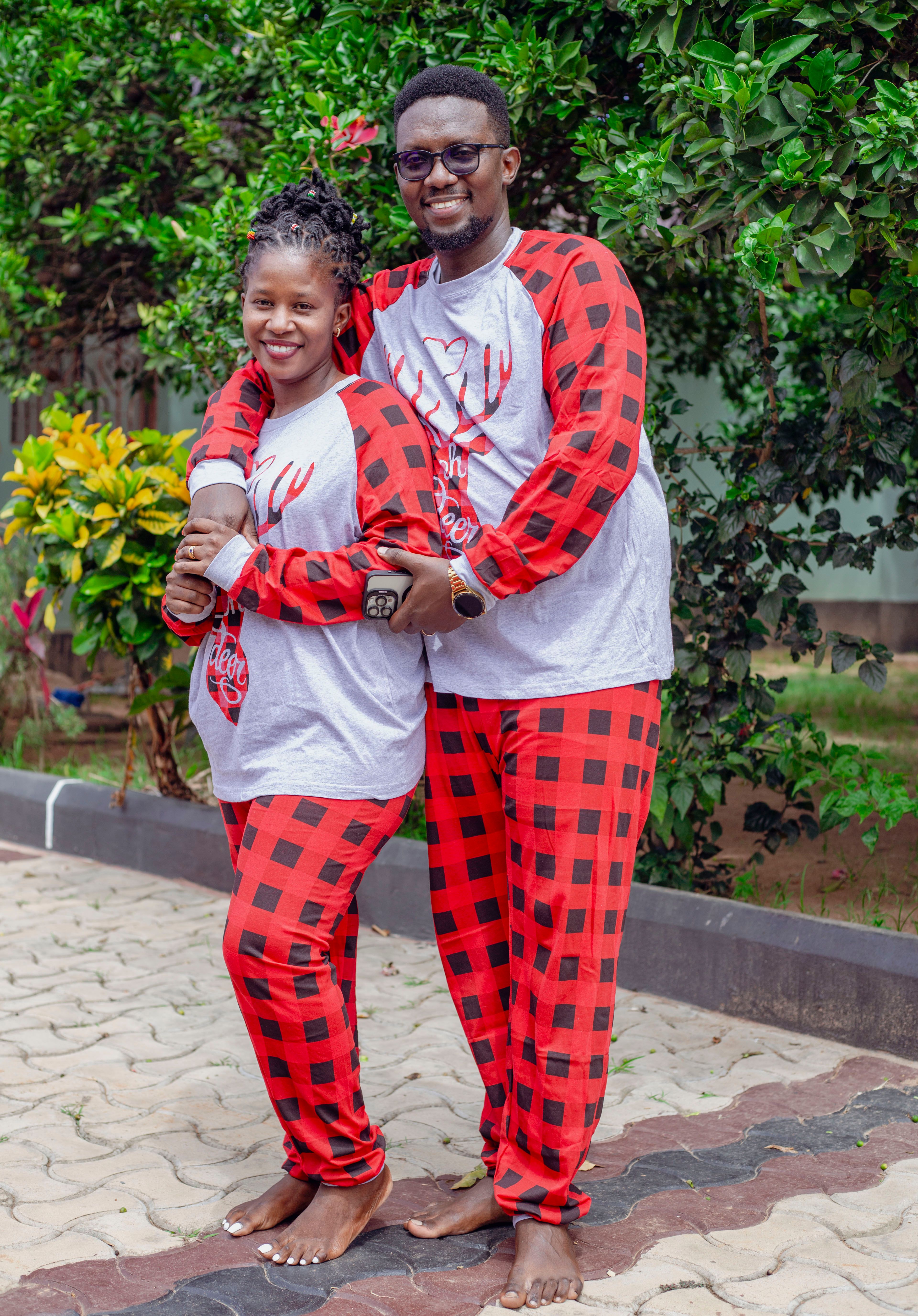 Smiling couple in matching red checkered pajamas outdoors, embracing in a garden setting.