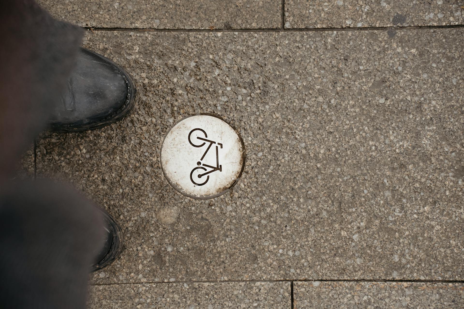 Street-level view of a bike path marker embedded in urban pavement with surrounding textures.