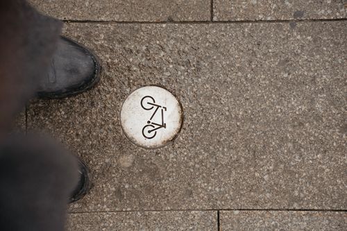 Free Street-level view of a bike path marker embedded in urban pavement with surrounding textures. Stock Photo