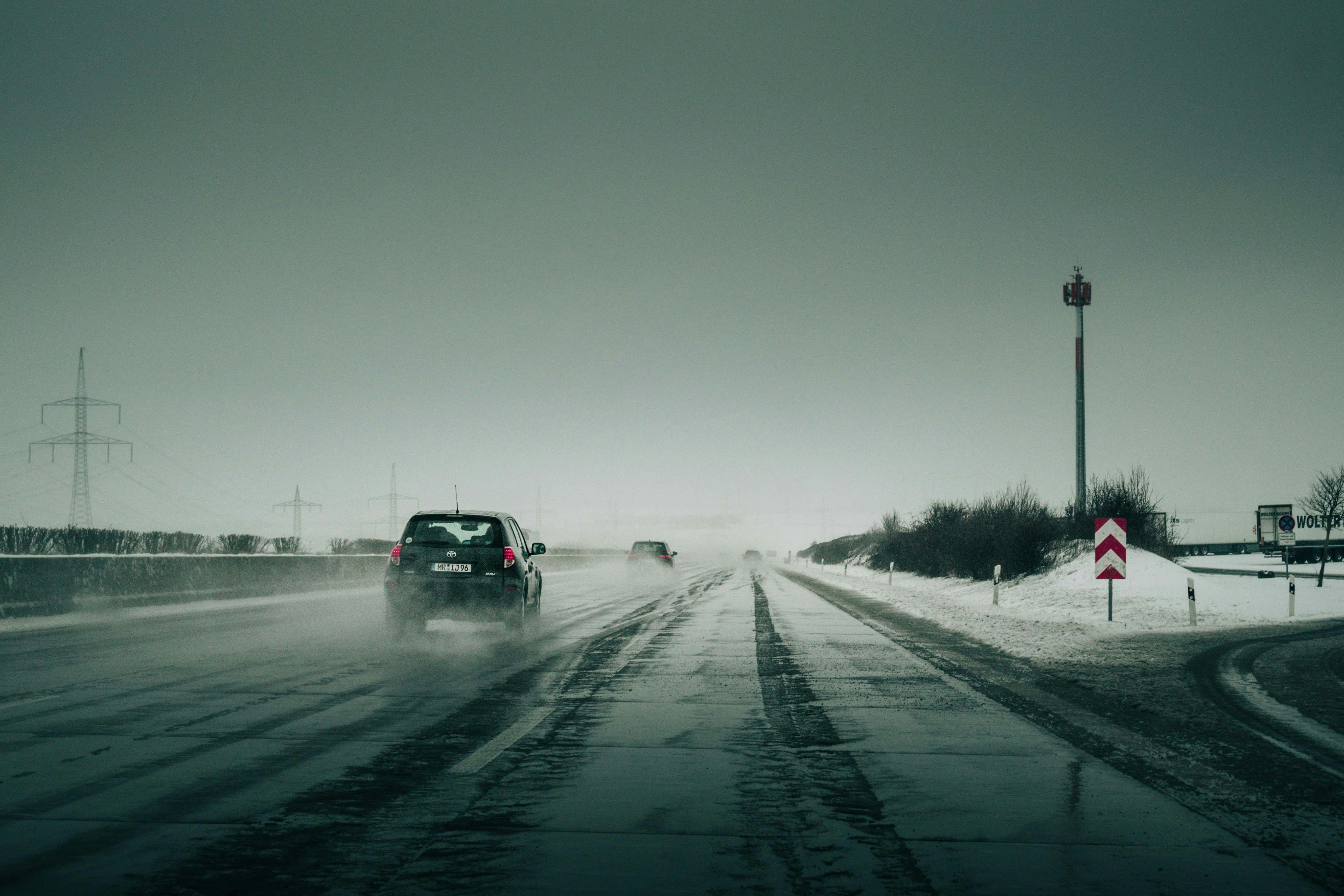 Car driving through snowy highway with fog, creating a mysterious atmosphere.