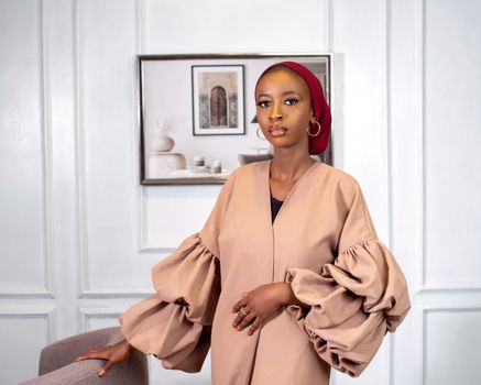 Stylish woman in beige jacket with red headscarf, elegant and modern indoors.