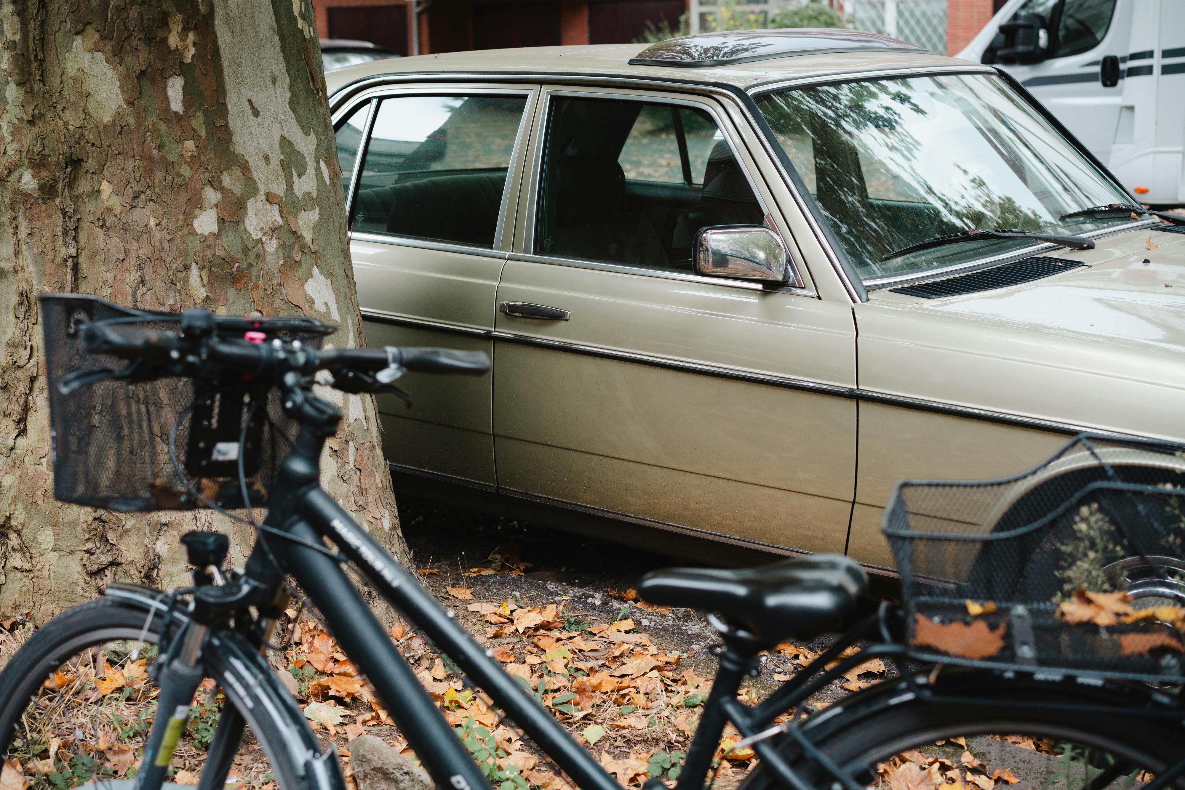 Gratis Escena urbana de otoño con un coche antiguo aparcado junto a una bicicleta en un entorno urbano, rodeado de hojas caídas. Foto de stock