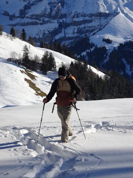 A solitary hiker with poles enjoys trekking through a snowy mountain landscape on a sunny day.