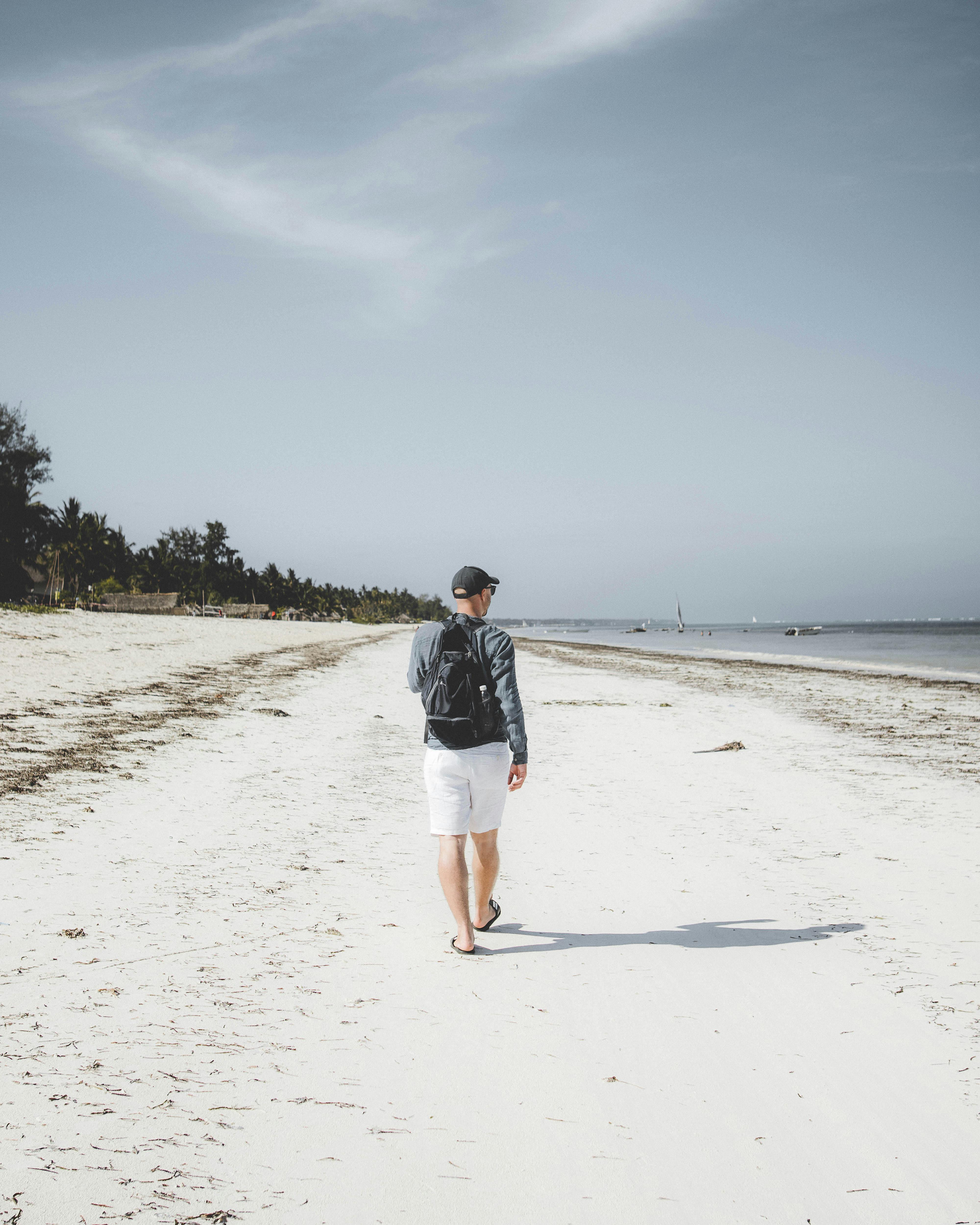 A man strolls along the pristine sandy beach in Zanzibar under a clear blue sky.