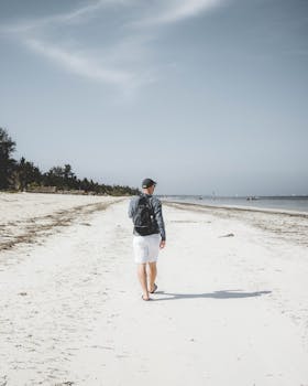 A man strolls along the pristine sandy beach in Zanzibar under a clear blue sky.