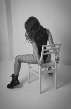 Black and white portrait of a woman in fishnets and boots, seated on a chair.