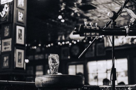 Artistic black and white photo of a pub setting with a guitar, microphone, and empty glass, capturing a moody ambiance.