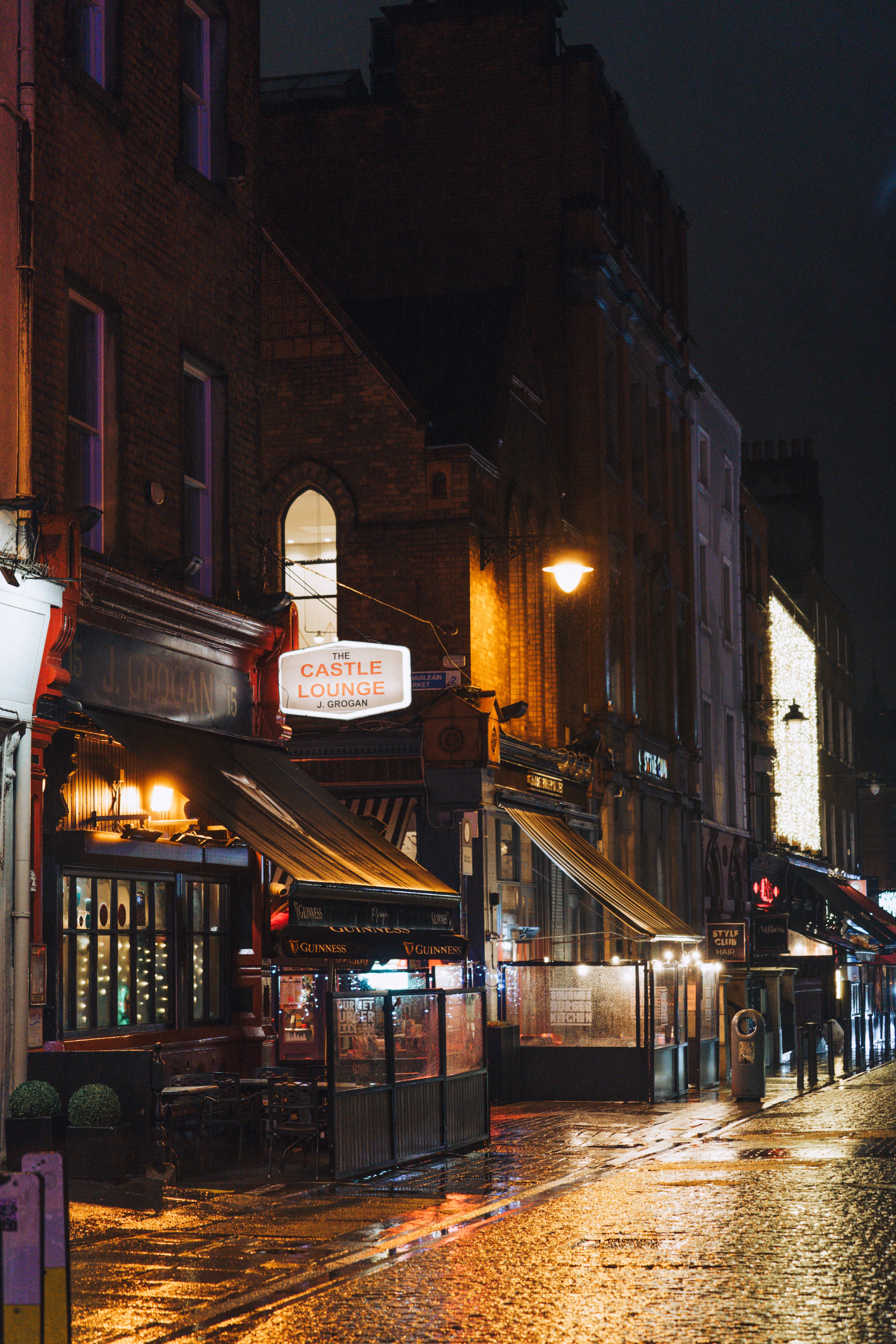 Rainy night view of a cozy Dublin street with lit pubs and wet cobblestones.