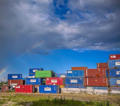 A stack of colorful shipping containers under a cloudy sky with a rainbow in Central Visayas, Philippines.