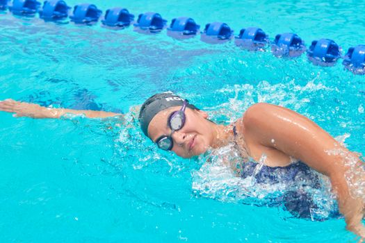 A woman practicing freestyle swimming in a bright blue swimming pool, exhibiting strong athletic skills.