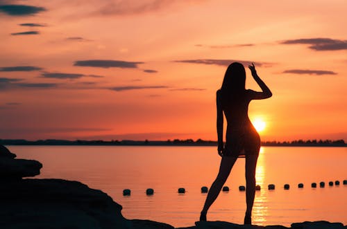 Silhouette of Woman Near Body of Water during Sunset