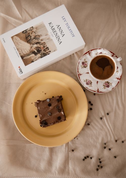 Free A warm setup featuring coffee, chocolate cake, and 'Anna Karenina' book. Stock Photo