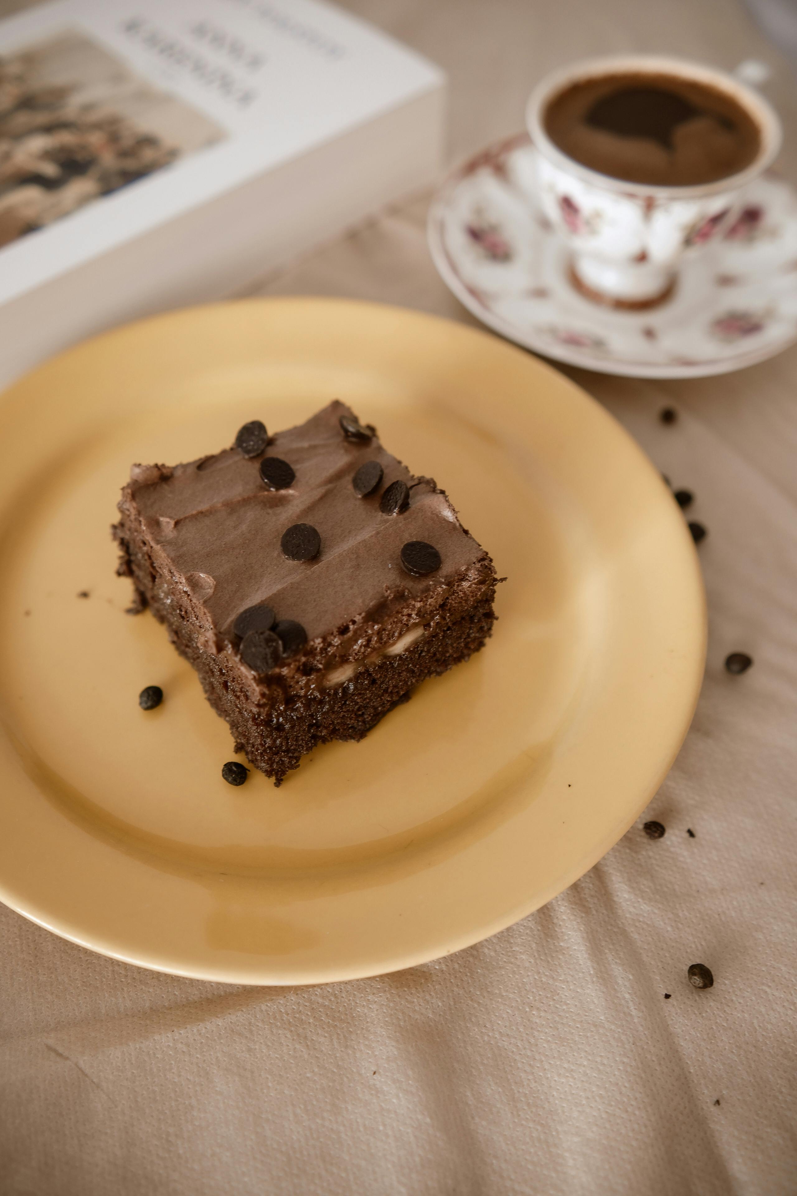 A delicious slice of chocolate cake and a cup of coffee next to a book, perfect for relaxation time.