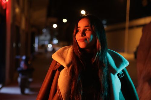 Free Portrait of a young woman in a coat enjoying the city lights at night. Stock Photo