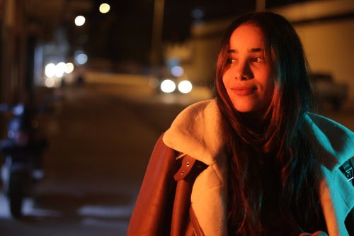 Free A woman smiles warmly under street lights, wearing a cozy jacket at night. Stock Photo