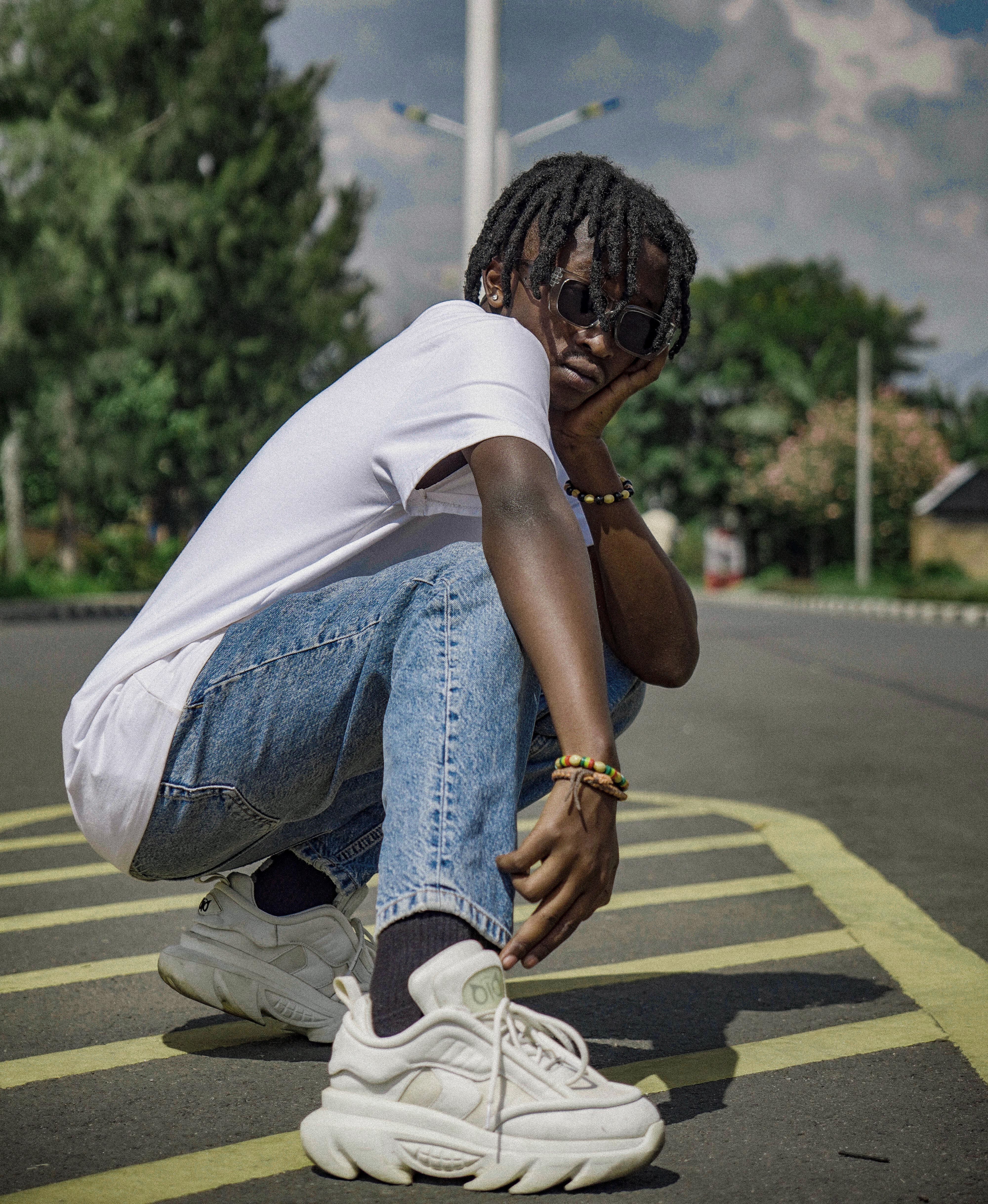 Young adult posing in urban street style with casual wear and sunglasses.