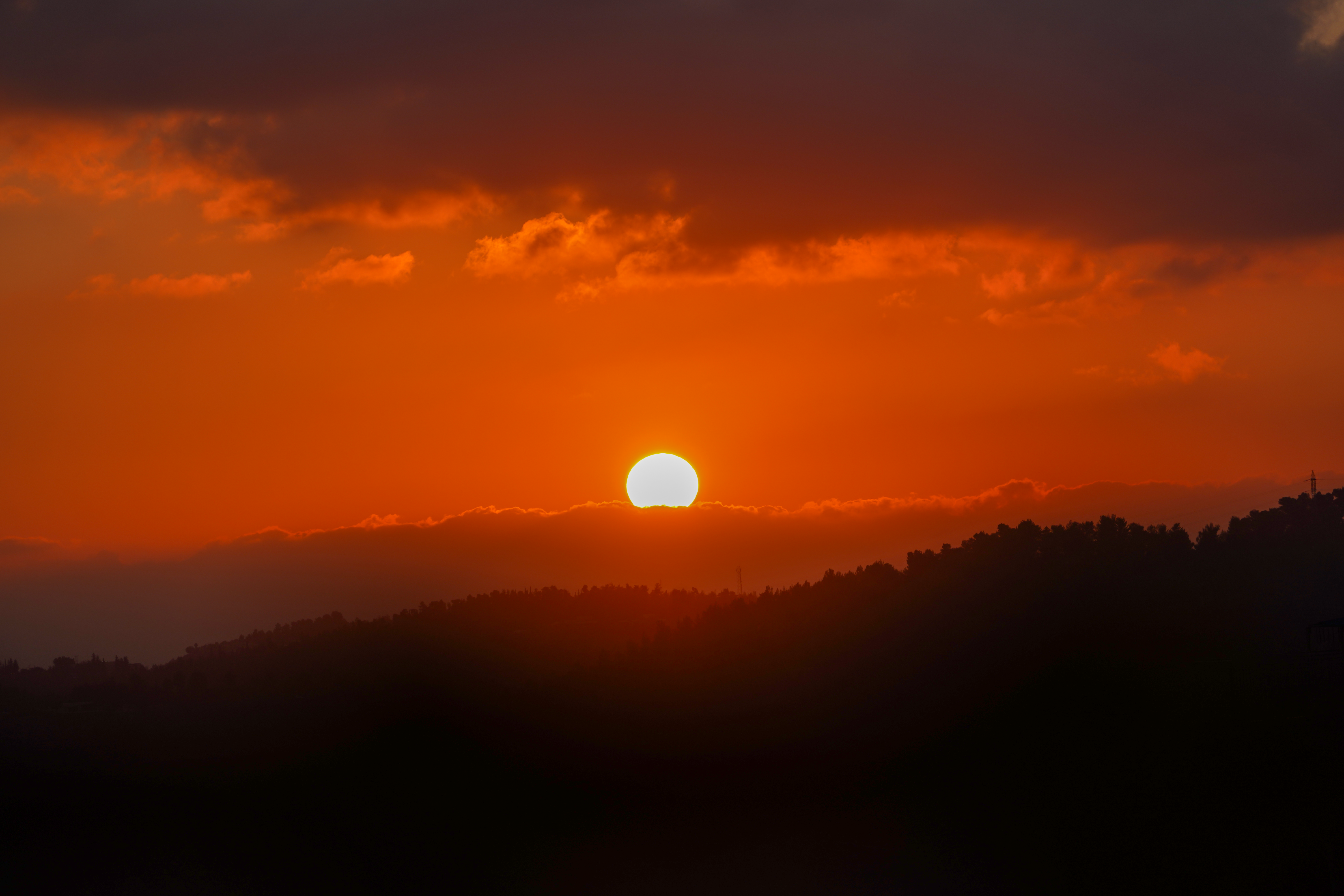 Captivating orange sunset with silhouetted hills and vibrant clouds in a serene atmosphere.
