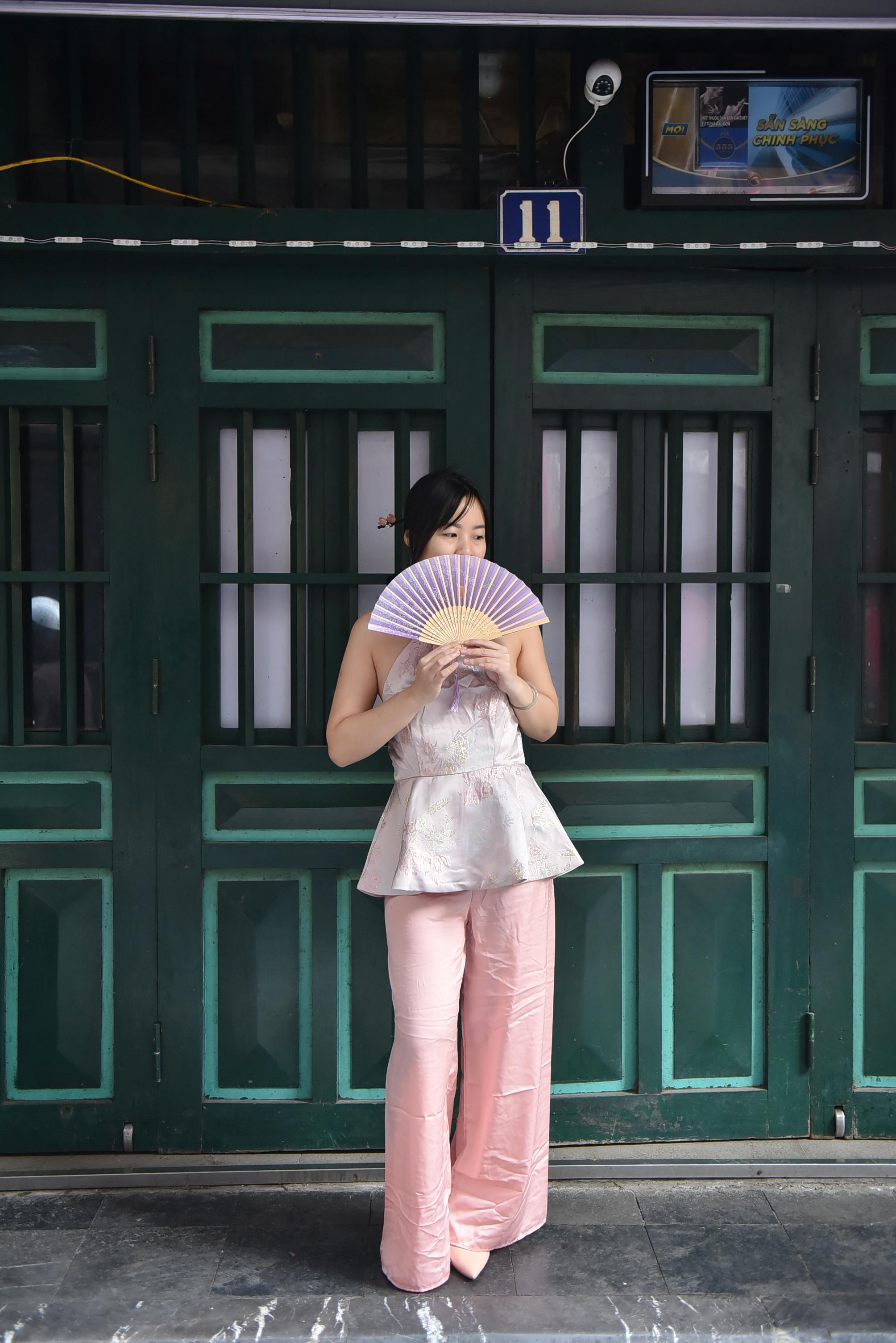 A woman stands with a fan in front of green doors.