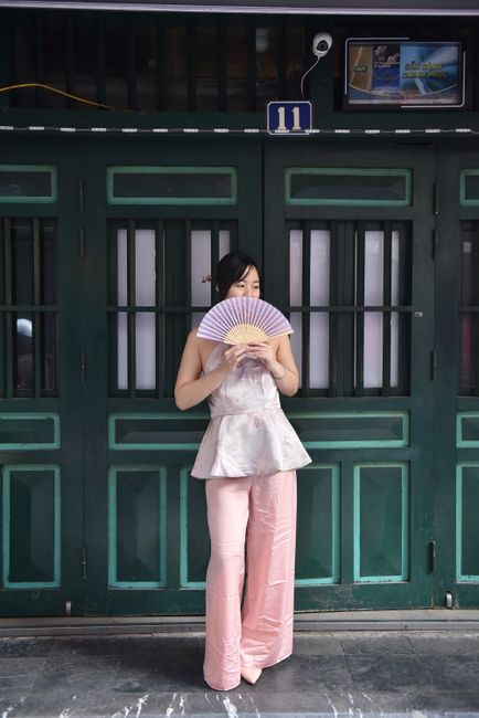 A woman stands with a fan in front of green doors.